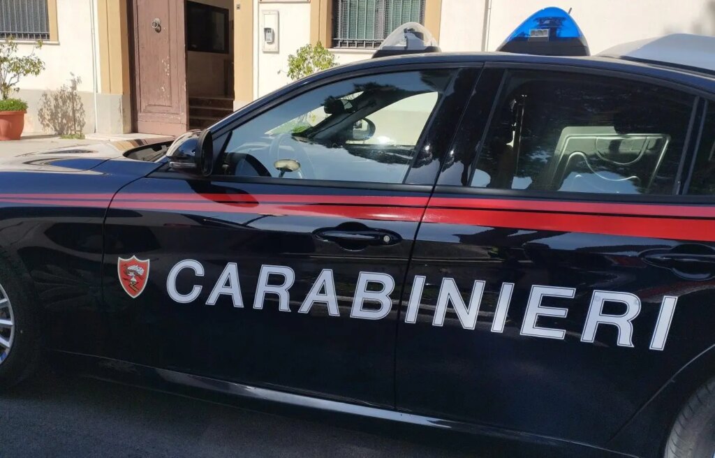 Side view of a black Italian Carabinieri patrol car with a red stripe and shield emblem on the door, parked on a street